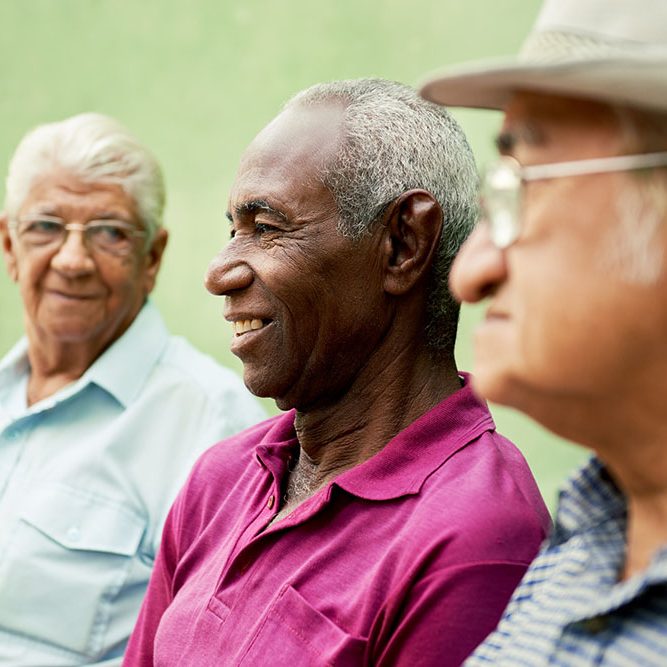 retired elderly people and free time, group of happy senior african american and caucasian male friends talking and sitting on bench in park
